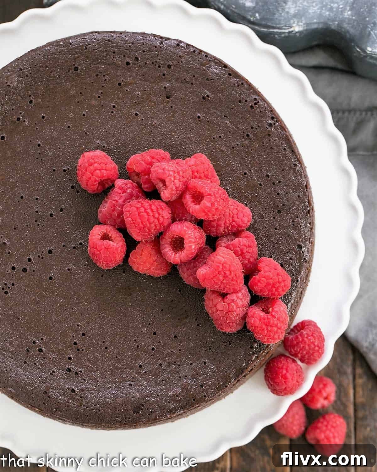 Overhead view of a beautifully garnished Flourless Chocolate Kahlua Cake, generously topped with fresh raspberries, sitting elegantly on a cake stand.