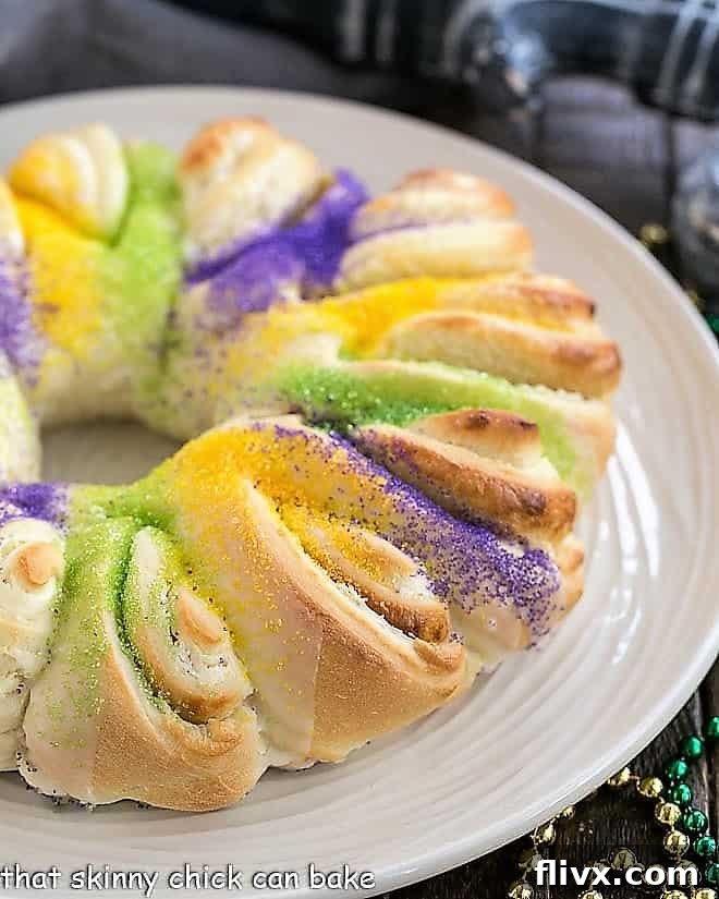 Easy King Cake with a rich cream cheese filling, beautifully decorated with yellow, green, and purple Mardi Gras sugars, presented on a pristine white plate.