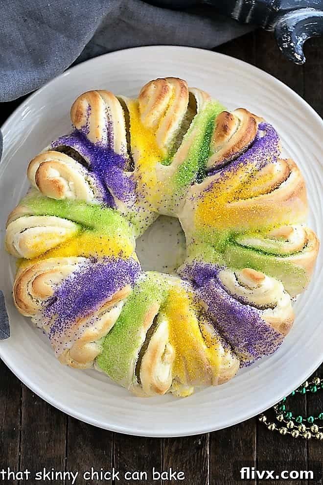 Overhead view of an Easy King Cake with cream cheese filling, adorned with traditional Mardi Gras colors, resting on a elegant round white serving dish.