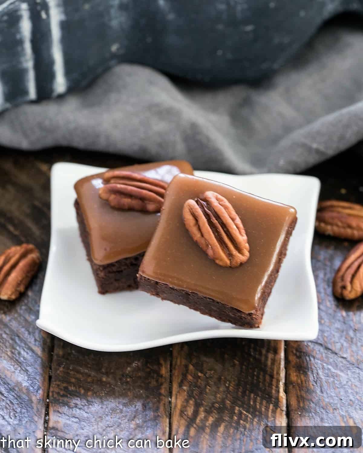 Two ultimate turtle brownies on a small white wavy plate, showcasing layers of fudgy chocolate, golden caramel, and crunchy pecans.