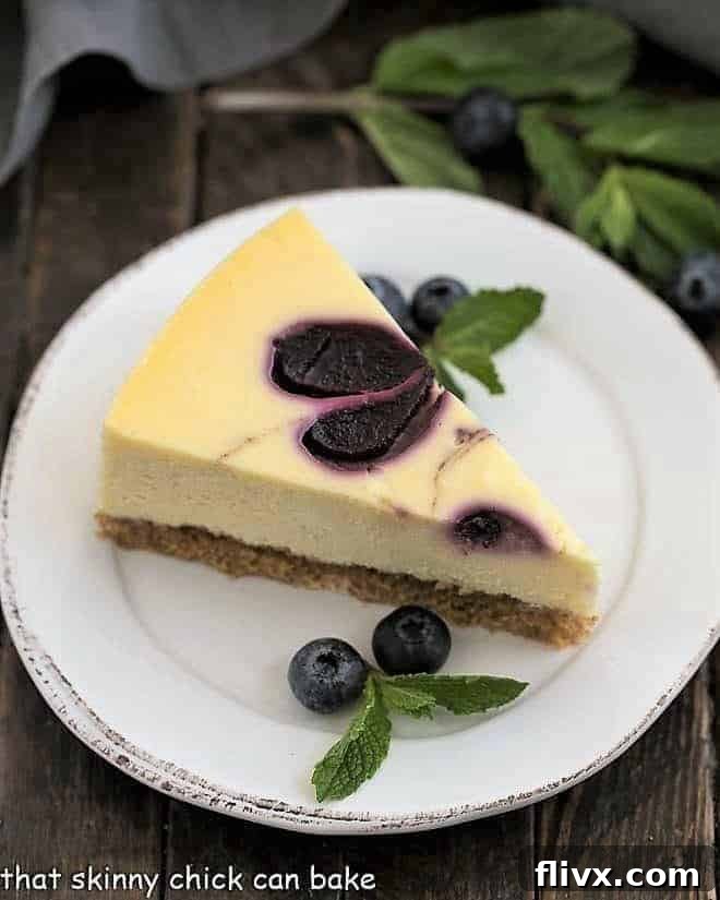 Slice of Blueberry Swirl Cheesecake on a white plate with mint and fresh blueberries, ready to eat and perfectly swirled.