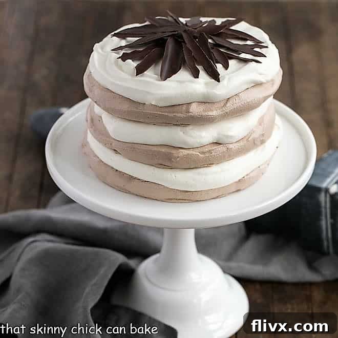 Layered Chocolate Meringue Cake on a white ceramic cake plate, adorned with chocolate shards