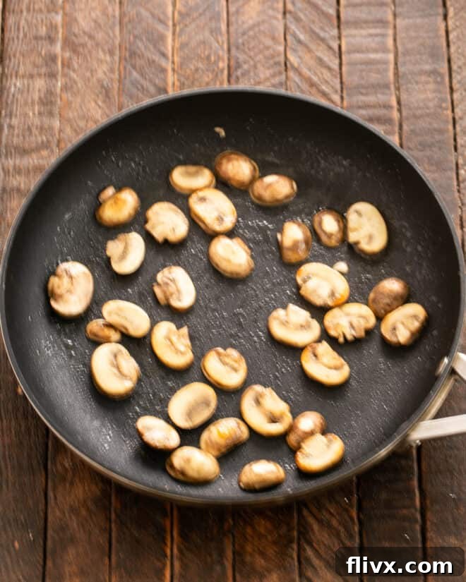 Sliced mushrooms being sautéed in a skillet with butter.
