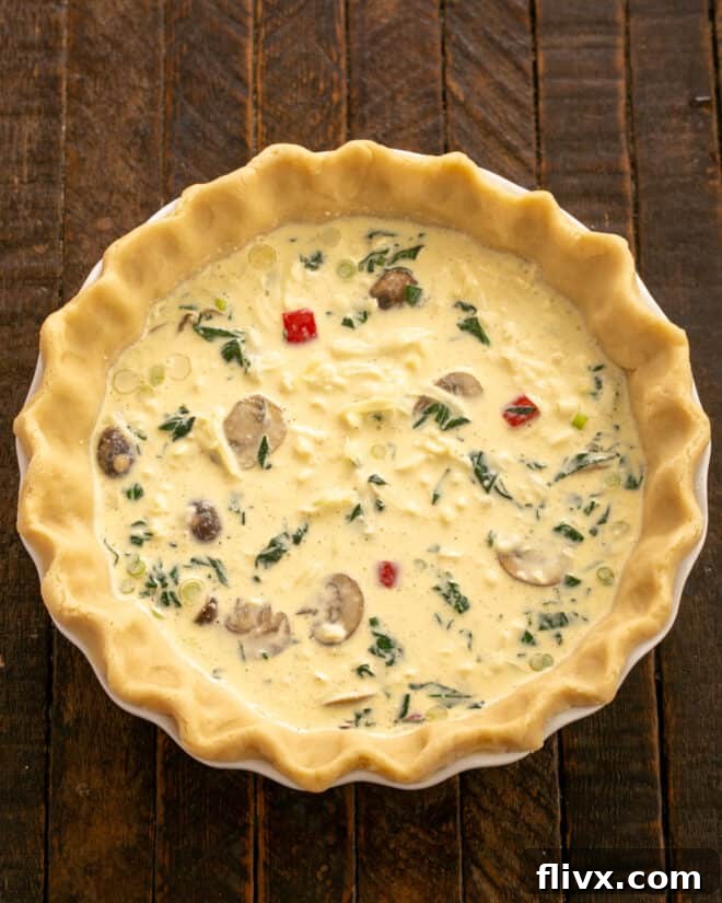 An unbaked pastry shell filled with sautéed vegetables, shredded cheese, and egg custard, ready for baking.