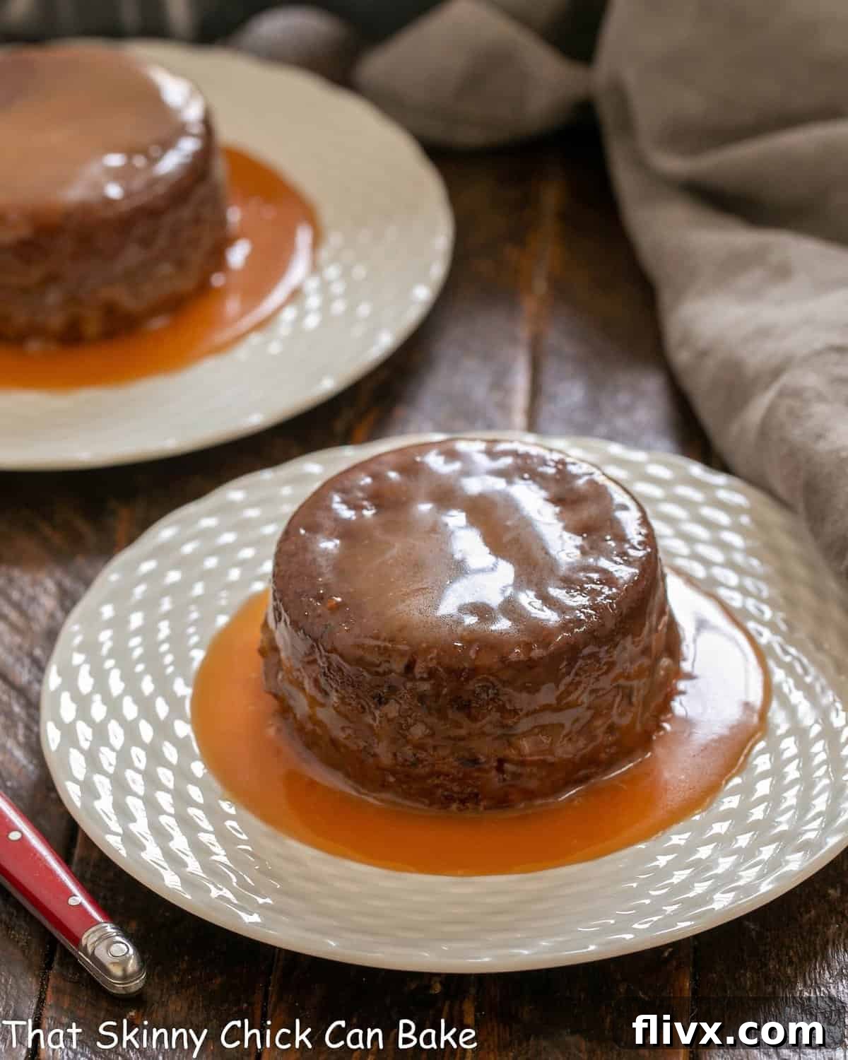 Two individual sticky toffee pudding cakes on white dessert plates, generously drizzled with golden caramel sauce, ready to be enjoyed.