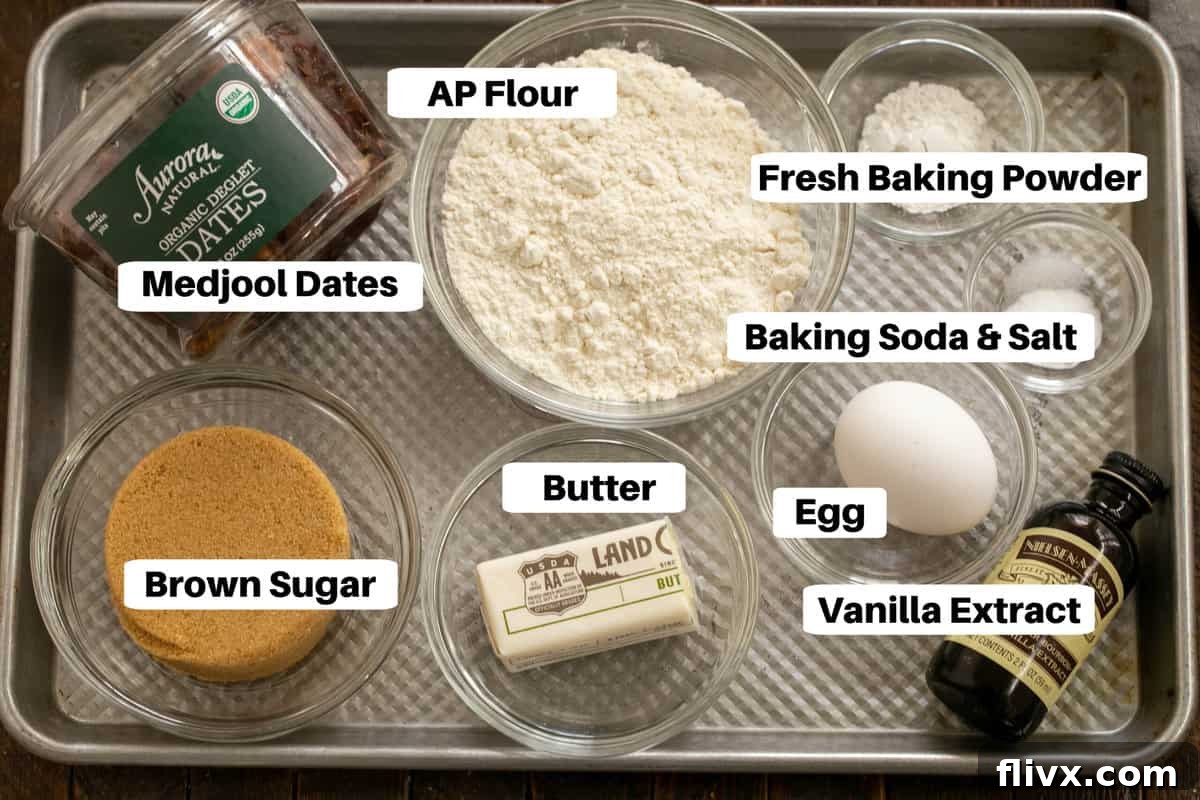 A collection of ingredients for sticky toffee pudding, including flour, sugar, eggs, and dates, neatly arranged on a metal sheet pan.