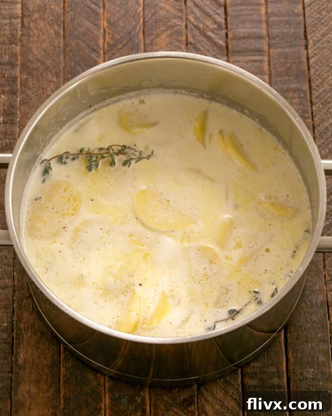 Cream, milk, seasonings, and sliced potatoes simmering in a pot.