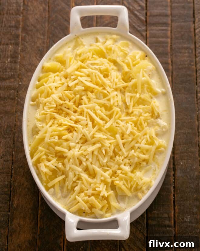 Potato mixture being transferred to a baking dish and topped with shredded cheese.