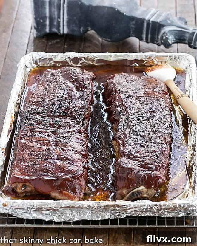 Two racks of perfectly glazed baby back ribs on a sheet pan, glistening with BBQ sauce after being broiled to perfection.