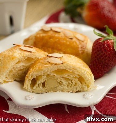 Homemade Almond Croissants - made from scratch, these exquisite croissants taste like they're from a French bakery! Homemade Almond Croissants on a white decorative plate with a strawberry. A vision of flaky, golden-brown perfection.