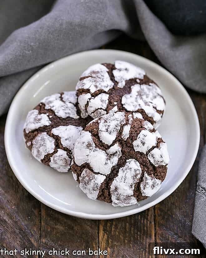 Overhead view of 3 fudgy chocolate earthquake cookies on a round white plate, showcasing their distinctive powdered sugar coating and deep chocolate cracks.