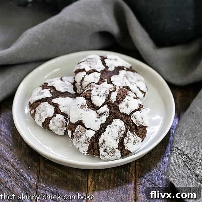 Fudgy Chocolate Earthquake Cookies on a white dessert plate, showing their powdered sugar coating and deep cracks