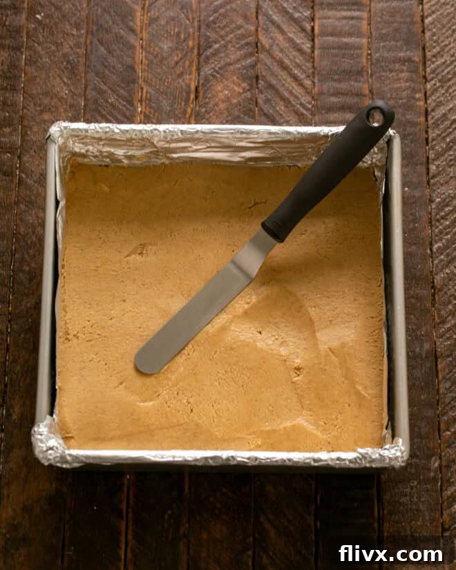 Step 4: Firmly pat the peanut butter mixture into the bottom of the prepared pan, creating an even layer.