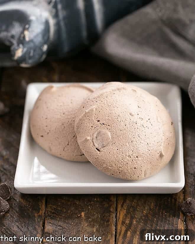 Two perfectly baked Chocolate Chip Meringues, showcasing their crisp texture, resting on a clean, square white plate.