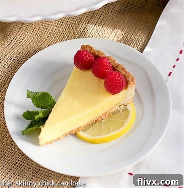 A perfectly sliced Tarte au Citron, also known as French Lemon Tart, elegantly garnished with vibrant red raspberries, showcasing its creamy yellow filling.