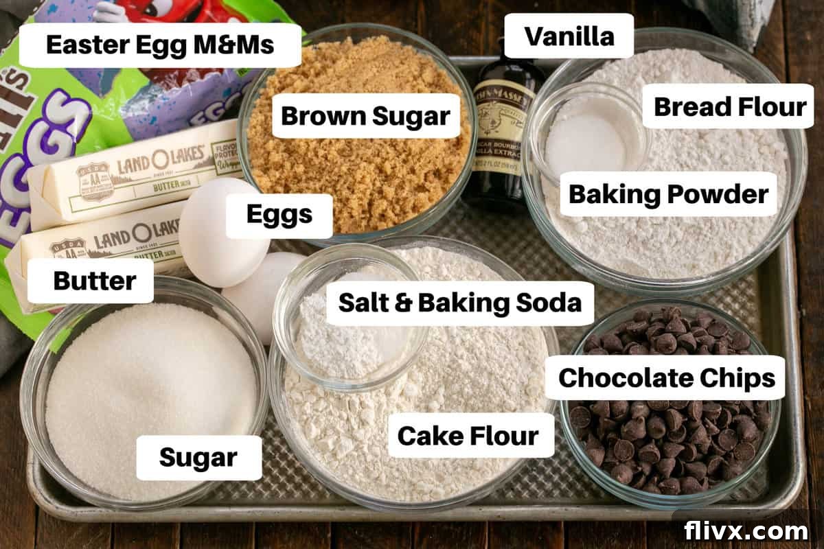 A neatly arranged flat lay of all labeled ingredients required for making Easter Egg Cookies, including flours, sugars, butter, chocolate chips, and colorful M&M's, ready for baking.
