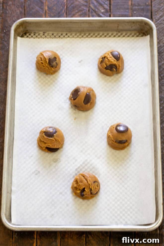 Scooped cookie dough balls arranged on a parchment-lined baking sheet, ready for baking.