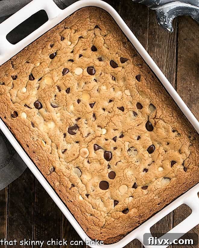 Overhead view of baked cookie bars in a white ceramic baking pan, glistening with melted chocolate.