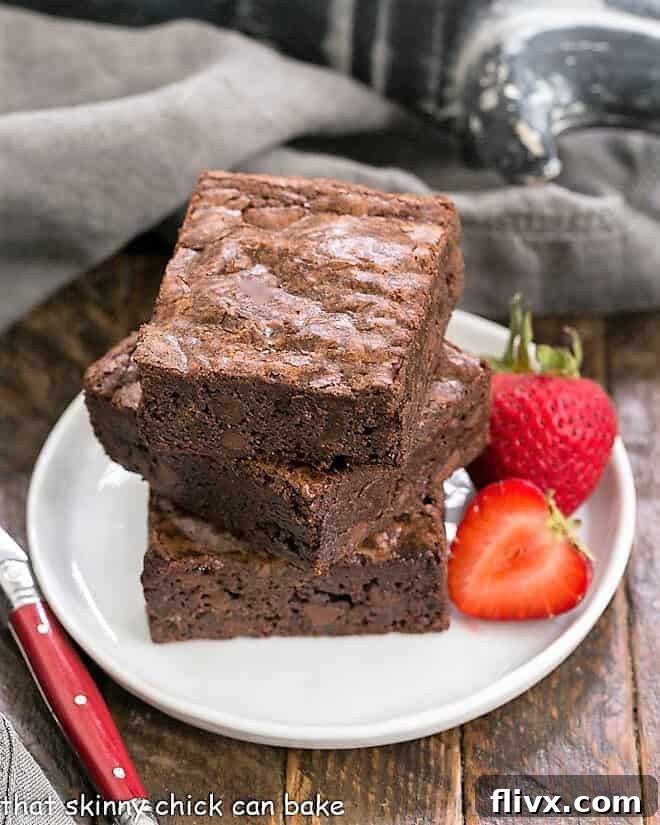 A stack of 3 homemade sheet pan brownies on a small white plate, showcasing their fudgy texture and shiny crust.
