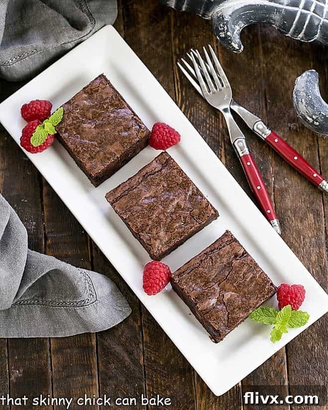 3 sheet pan brownies on a white tray with raspberries and mint garnish, highlighting their elegant presentation.