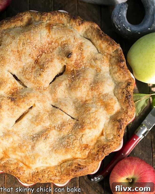 Overhead view of whole Caramel Apple Pie with apples and a red handle knife.