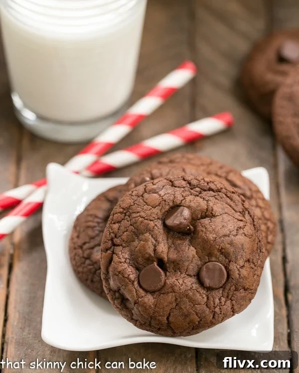 Decadent Triple Chocolate Cookies arranged on a square white plate, accompanied by cheerful red and white straws and a frosty glass of milk, inviting a delightful indulgence.