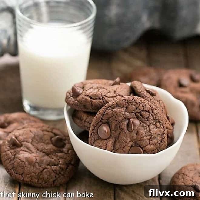 A generous serving of Triple Chocolate Cookies nestled in and around a white ceramic bowl, paired with a refreshing glass of milk, highlighting their inviting texture and rich color.