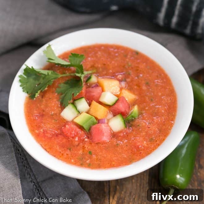 A white bowl of Watermelon Gazpacho garnished with cubes of avocado, melon, and cucumber.
