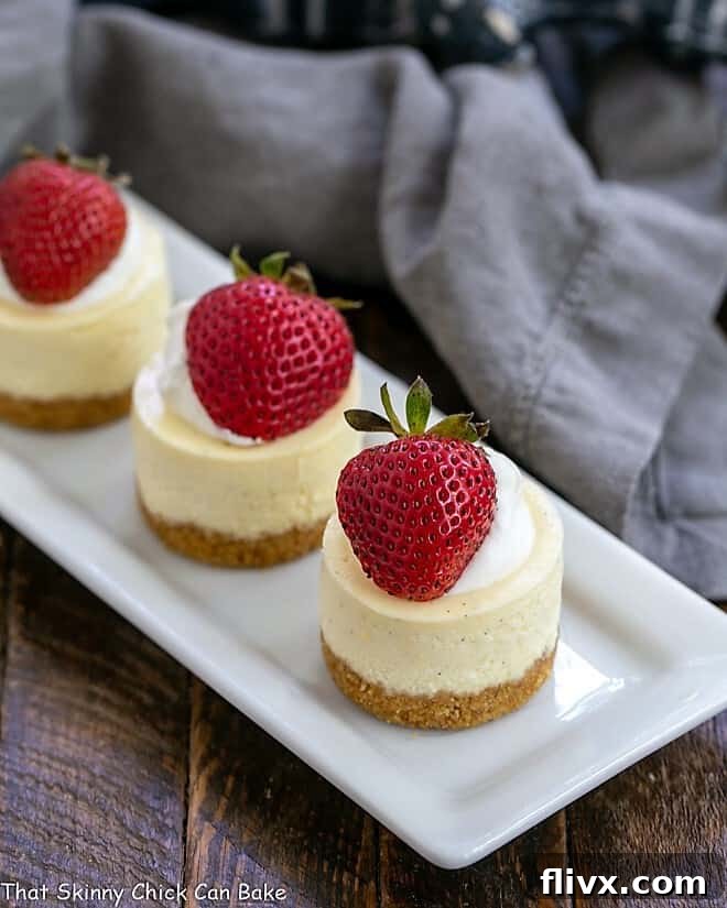 Vanilla Bean Mini Cheesecakes topped with strawberries and cream on a white platter, ready to be served at a special event.
