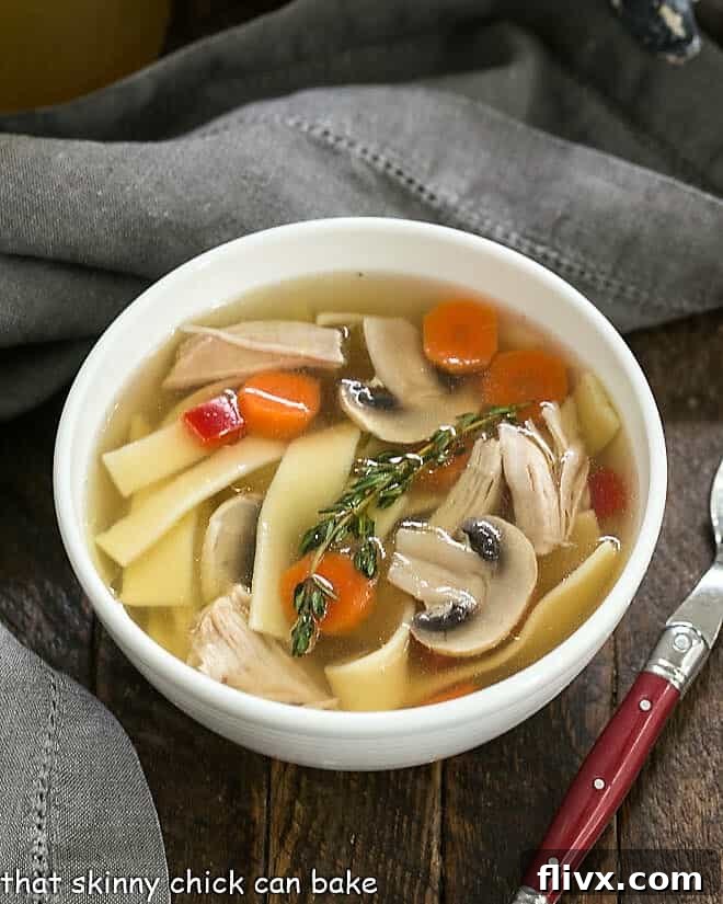 A comforting bowl of homemade chicken stock with tender carrots, noodles, and shredded chicken pieces, perfectly showcasing its rich golden hue.
