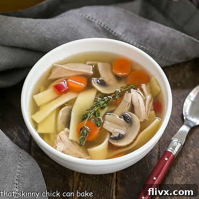Overhead shot of a inviting bowl of homemade chicken stock with noodles and vegetables, garnished with a red-handled spoon, showcasing a wholesome and comforting meal.