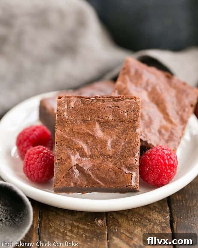 Best Fudgy Brownies - an extra step makes these dreamy and irresistible! Best Fudgy Brownies on a round dessert plate with raspberries to garnish, showcasing their rich, dark color and crackly top.