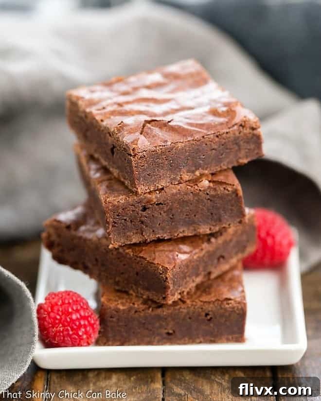 Best Fudgy Brownies - an extra step makes these dreamy and irresistible! Best Fudgy Brownies stacked neatly on a white square plate, showing their thick, decadent texture.