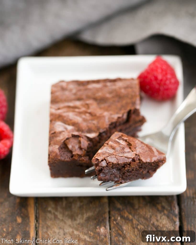Best Fudgy Brownies - an extra step makes these dreamy and irresistible! Best Fudgy Brownies on a square plate with a fork removing a bite, showing the dense, moist interior.