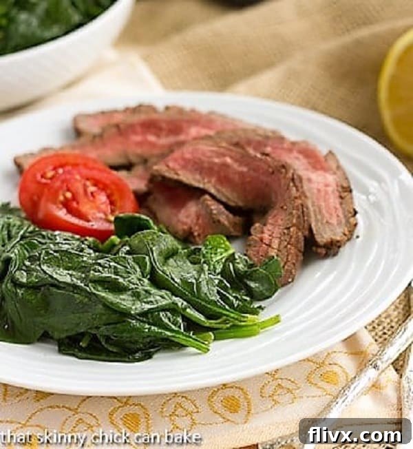 Easy Lemon Spinach served alongside a perfectly cooked flank steak on a white plate, showcasing a complete and healthy meal.