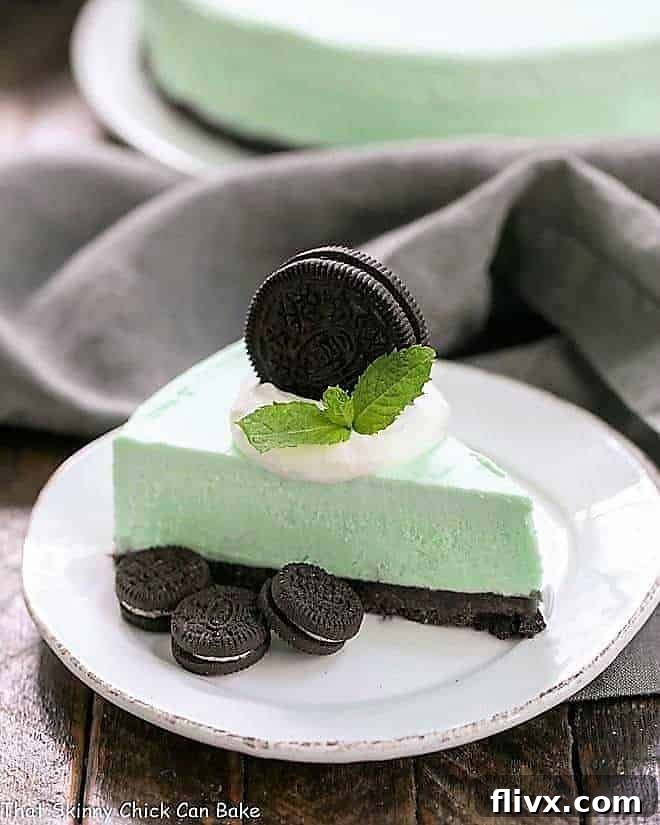 A beautifully presented slice of Frozen Grasshopper Pie with an Oreo Crust on a small round white plate, garnished with whipped cream and a mini Oreo.