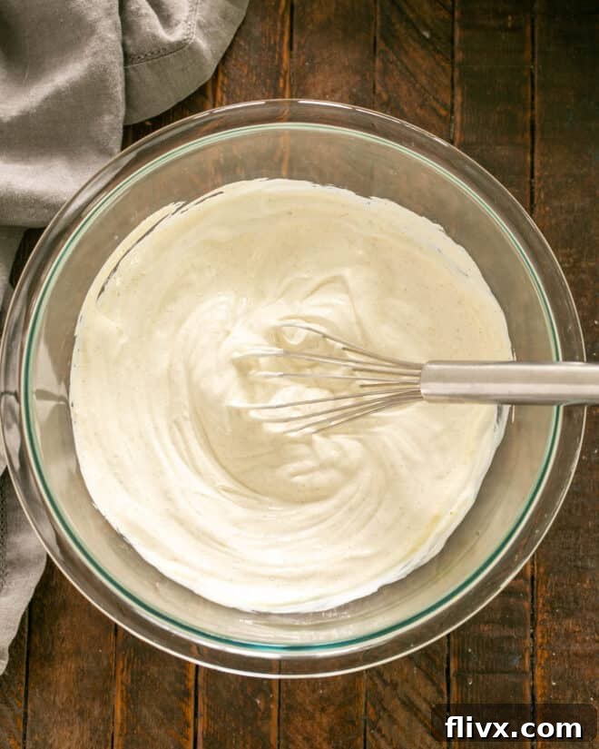 A close-up shot of mayonnaise and sour cream being whisked together in a mixing bowl, creating a smooth, creamy base for the dip.