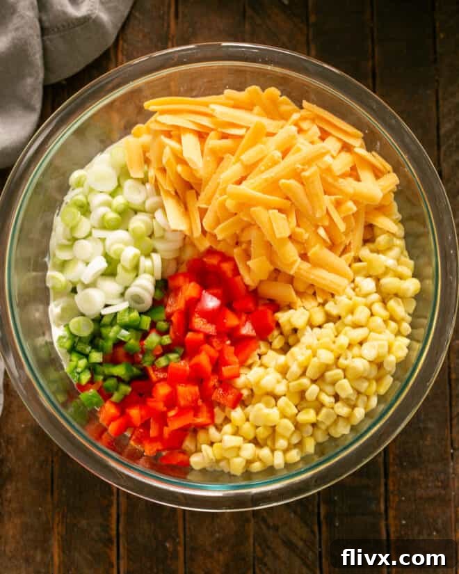All the remaining ingredients for the corn dip, including corn, bell pepper, cheese, and spices, are gathered in a large mixing bowl, ready for combining.