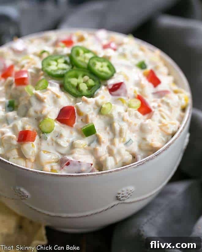 A delicious Sour Cream Corn Dip viewed from the side, presented in a crisp white ceramic bowl and elegantly garnished with fresh jalapeño slices.