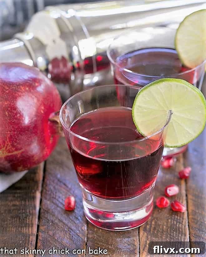 Two Pomegranate Cosmopolitan Cocktails in high ball glasses, garnished with lime twists.