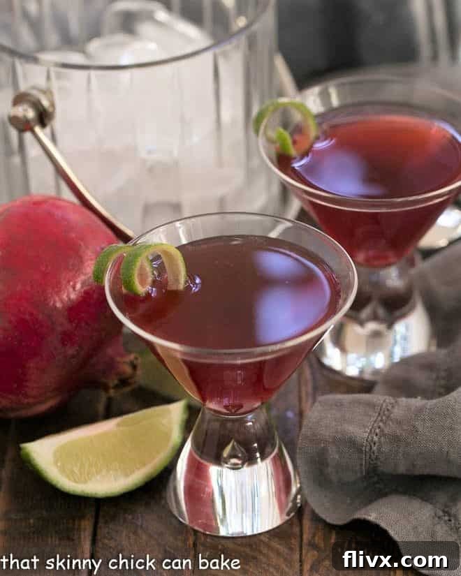 Two Pomegranate Cosmopolitan Cocktails in martini glasses with lime twists, ready to be served.