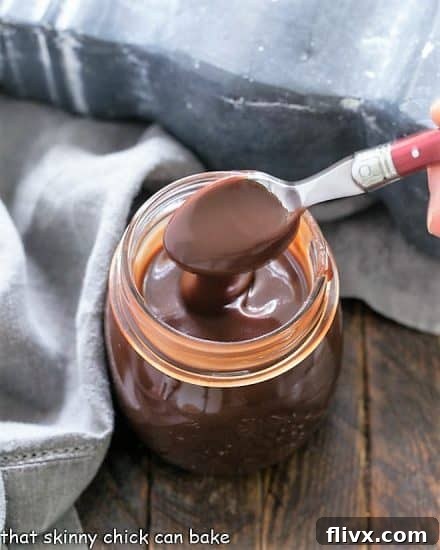 Rich and luscious Homemade Fudge Sauce! The perfect topping for ice cream and more, ready for your next dessert creation! A glass jar filled with luscious, homemade hot fudge sauce, with a spoonful being removed, showcasing its thick and rich texture.
