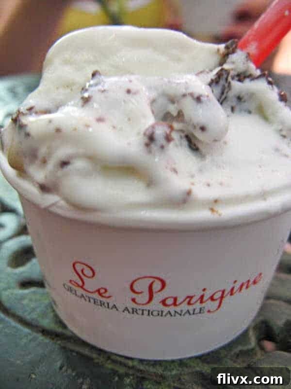 Hot fudge sauce: The perfect decadent topping, even after a failed attempt at homemade Italian gelato! A paper cup filled with half pignoli and half stracciatella gelato, held against a charming Italian street scene in Florence.