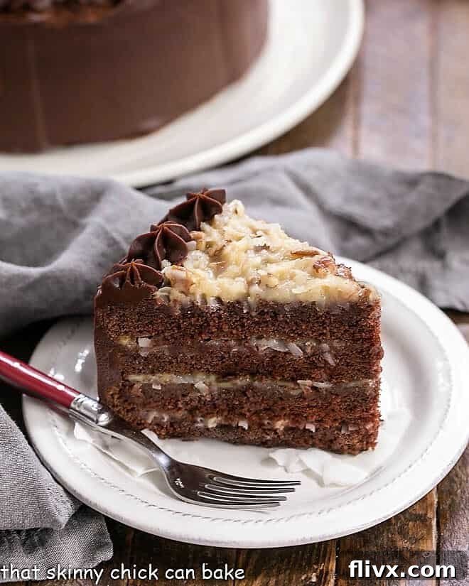A perfectly sliced piece of German Chocolate Cake on a white plate, with the multi-layered cake in the background.