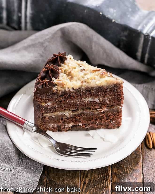 Slice of German Chocolate Cake on a dessert plate with a red fork, showcasing layers and filling.