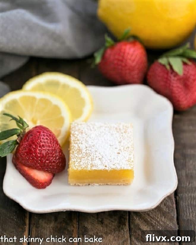 White dessert plate with the Best Lemon Bars, garnished with fresh strawberry slices and vibrant lemon slices, highlighting their bright color.