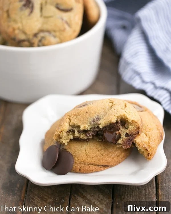 The New York Times Chocolate Chip Cookies with one broken open on a white square plate, revealing gooey chocolate.
