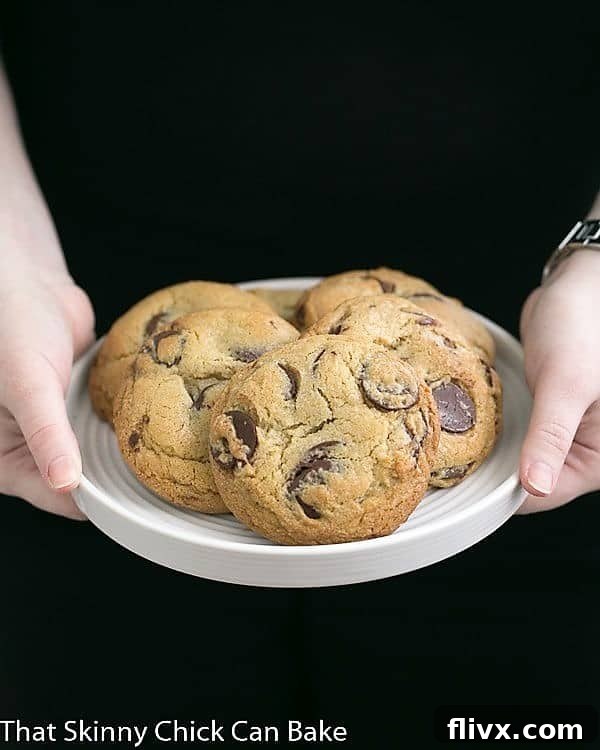 Jacques Torres' Secret Chocolate Chip Cookies on a white plate held by a girl's hands, highlighting their inviting size and homemade appeal.