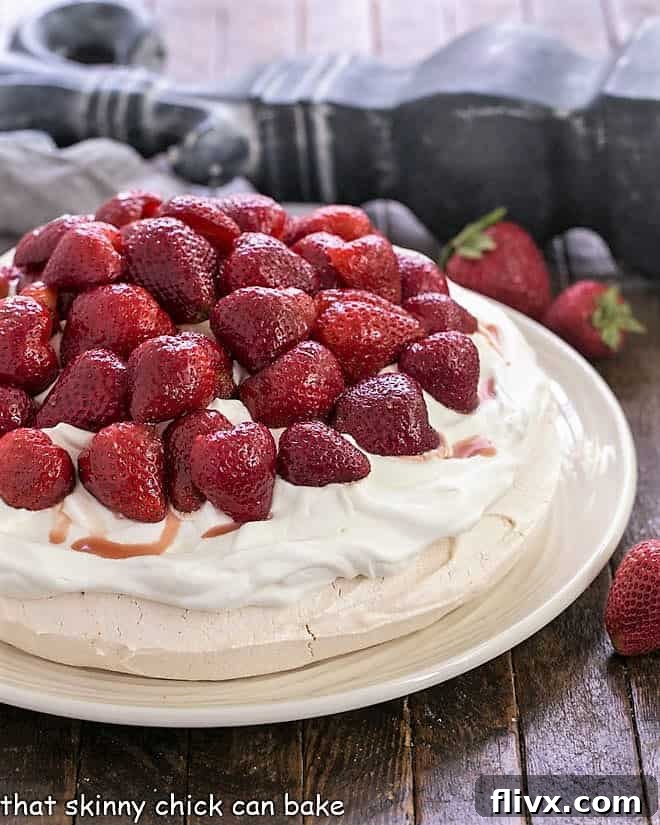 Strawberry Pavlova on a white serving plate topped with halved strawberries and whipped cream.