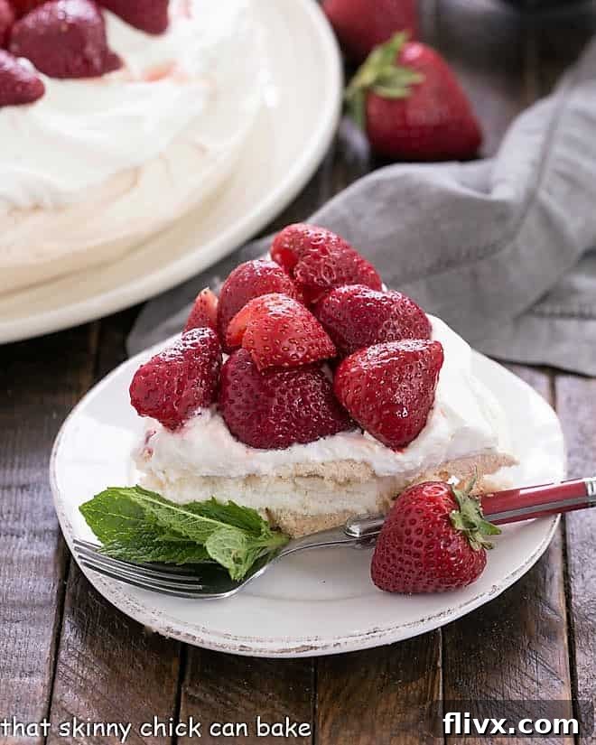 Slice of strawberry pavlova on a dessert plate garnished with fresh mint.